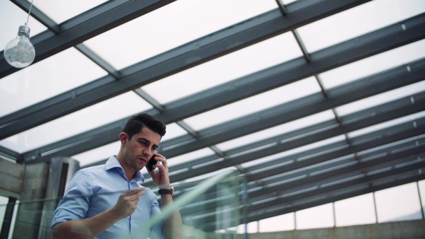 A young businessman with smartphone in corridor outside office, making a phone call. Slow motion.