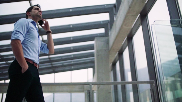 A young businessman with smartphone in corridor outside office, making a phone call. Slow motion.