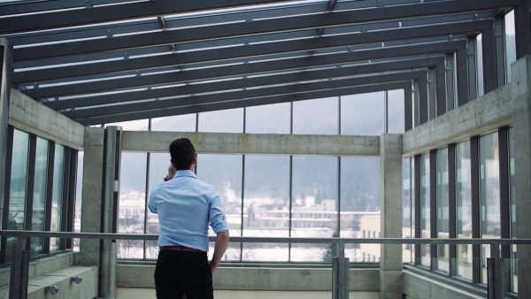 A rear view of young businessman with smartphone in corridor outside office, making a phone call. Slow motion.