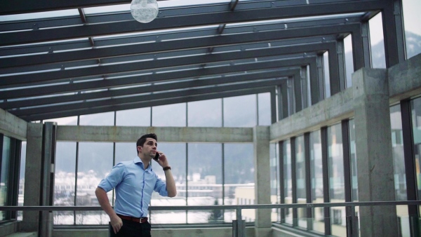 A young businessman with smartphone in corridor outside office, making a phone call. Slow motion.