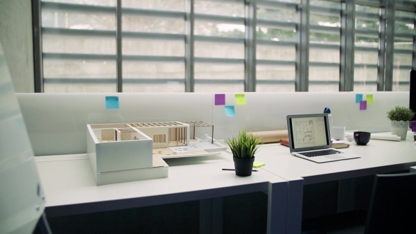 Laptop, blueprints on screens and model of a house in interior of office of architects. Slow motion.