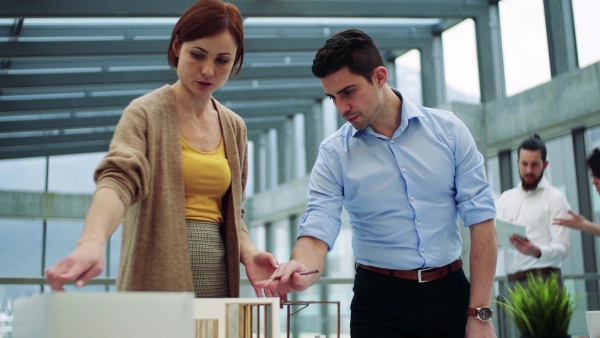 A group of young architects with model of a house standing in office, working and talking.