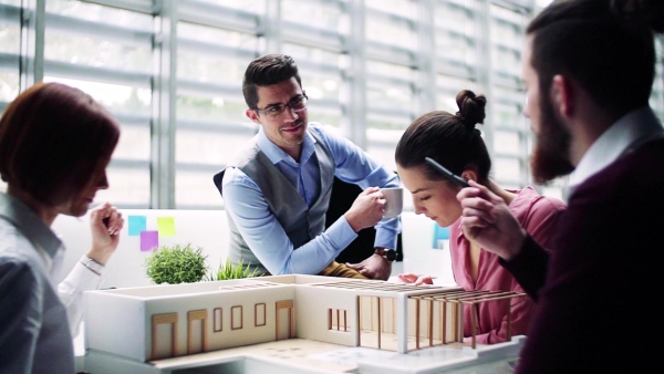 A group of young architects with model of a house in office, working and talking. Slow motion.