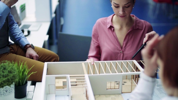 A group of young architects with model of a house in office, working and talking. Slow motion.