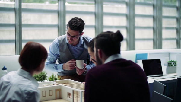 A group of young architects with model of a house in office, working and talking. Slow motion.