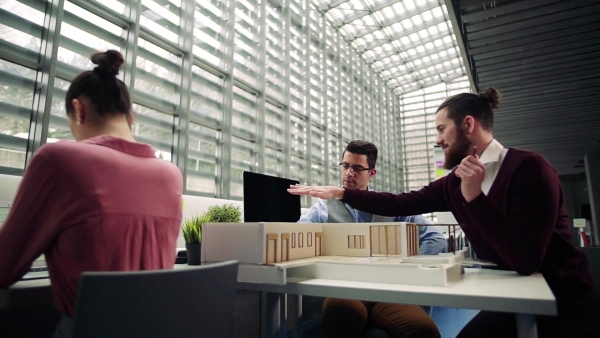 A group of young architects with model of a house in office, working and talking. Slow motion.