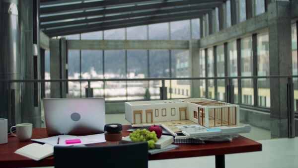 An interior of an office of an architect, laptop and model of a house on the desk.