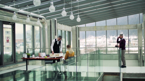 Group of architects with model of a house standing in office, working and talking.