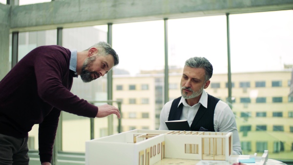 Two male architects with model of a house in office, working and talking.