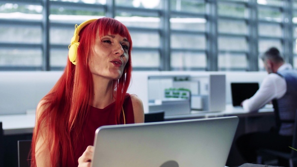 A mature woman with laptop and headphones in office, listening to music.