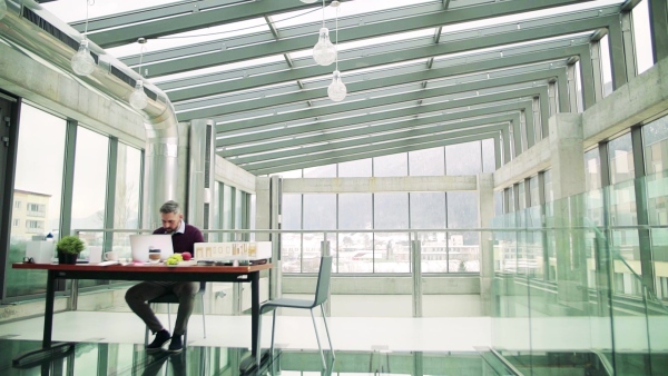 A mature architect with laptop and model of a house in office, working. Slow motion.