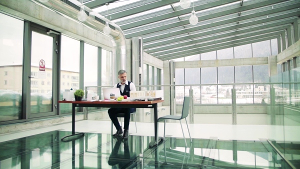 A mature architect with laptop and model of a house in office, working. Slow motion.