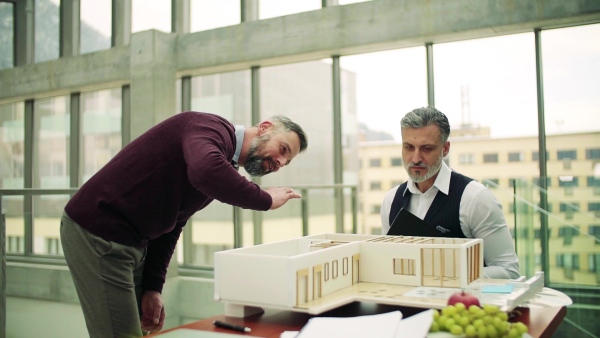 Two male architects with model of a house in office, working and talking. Slow motion.