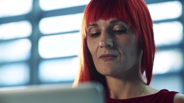 A close-up portrait of mature businesswoman sitting at desk in office, using laptop. Slow motion.