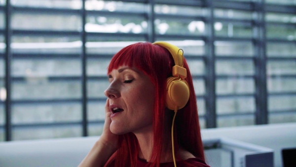 A mature woman with headphones in office, listening to music. Slow motion.