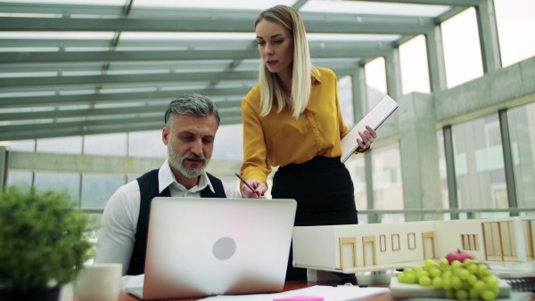 Two architects with model of a house in office, working and talking.