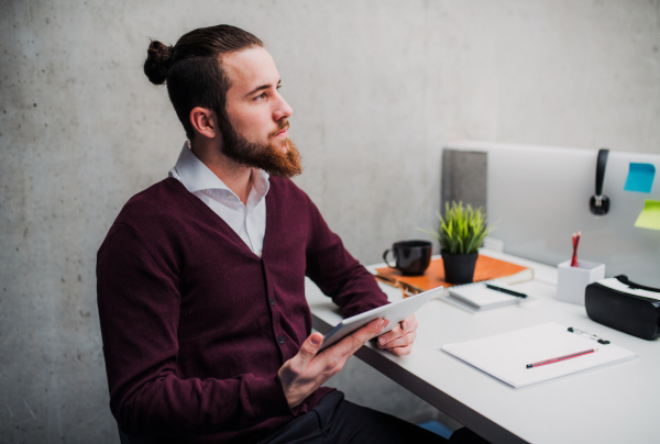 A young businessman with tablet sitting at the desk in office, working.