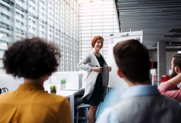 A group of young businesspeople listening to a presentation in office, talking.