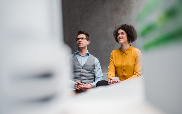 Two young businesspeople sitting in office, listening to a presentation. Copy space.