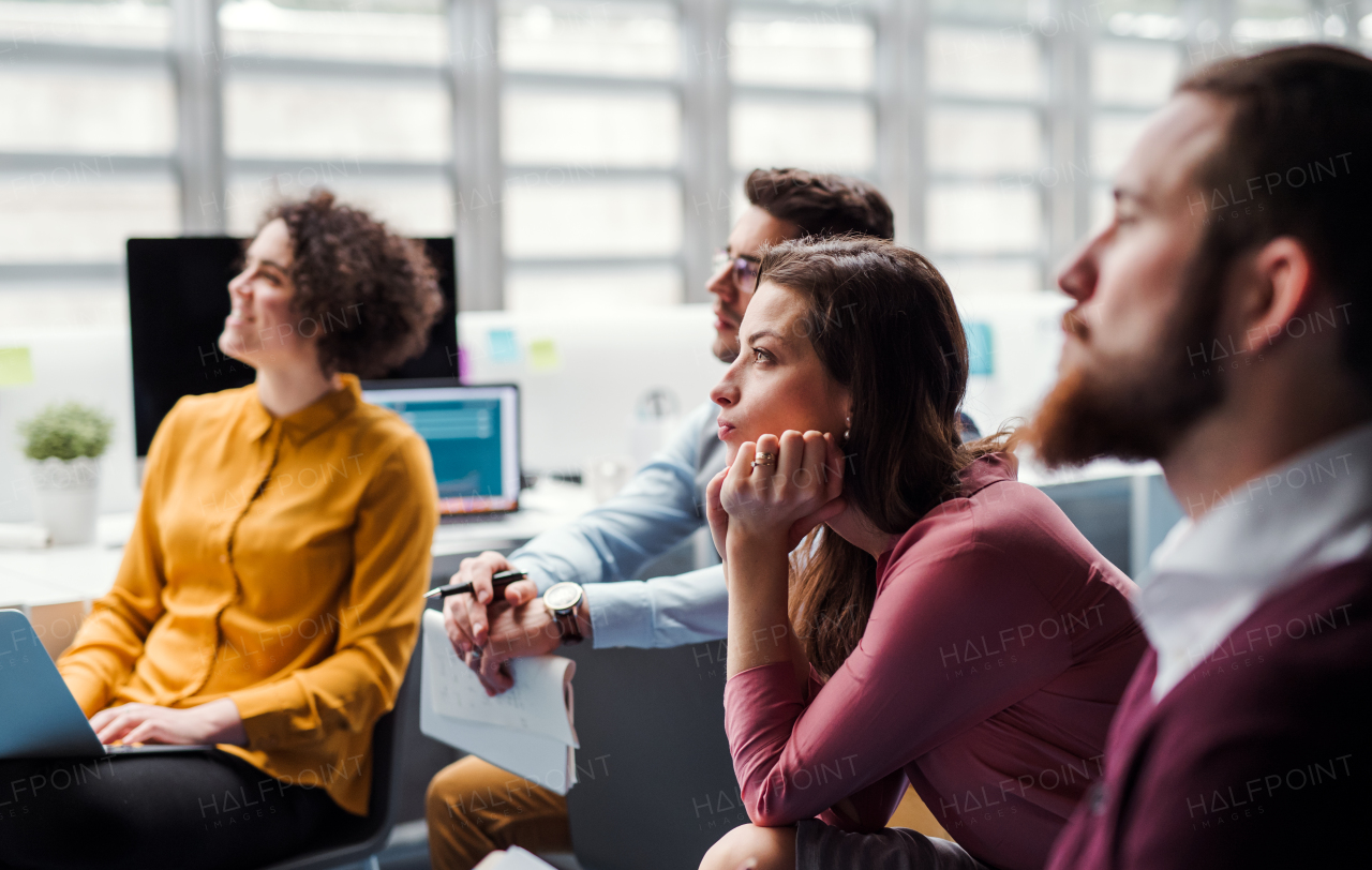 A group of young businesspeople in office, listening to a presentation.