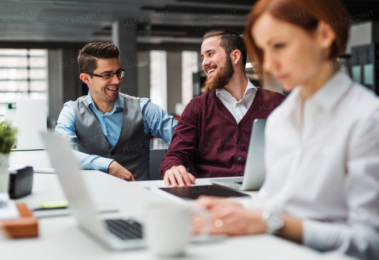 A group of young businesspeople with laptop working together in office, talking.