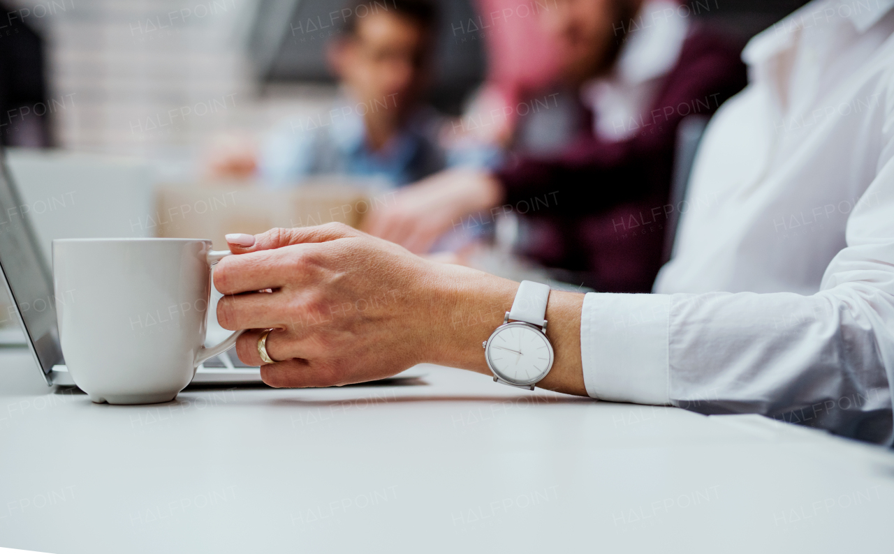 A midsection of businesswoman with a cup of coffee working in office, using laptop. A close-up.