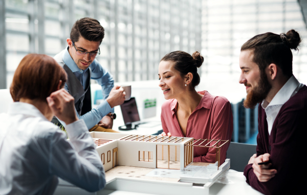 A group of young architects with model of a house working in office, talking.