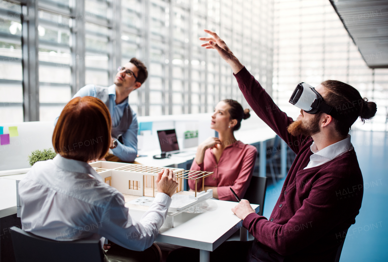 A group of young architects with model of a house and VR goggles working in office, talking.