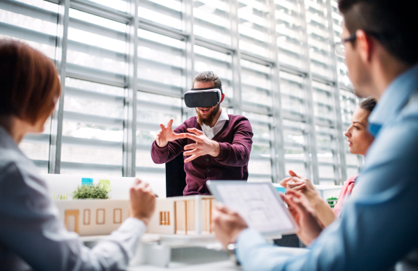 A group of young architects with model of a house and VR goggles working in office, talking.