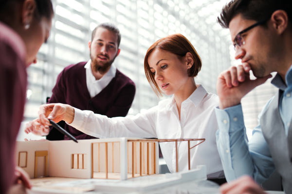 A group of young architects with model of a house working in office, talking.