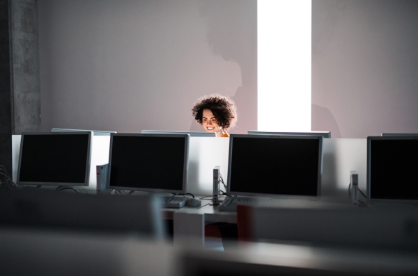 A cheerful young student sitting at the desk in a library, using computer. Copy space.