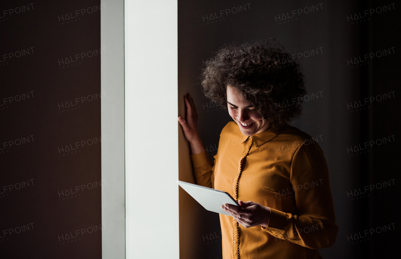 Portrait of a young cheerful businesswoman with tablet indoors in an office. Copy space.