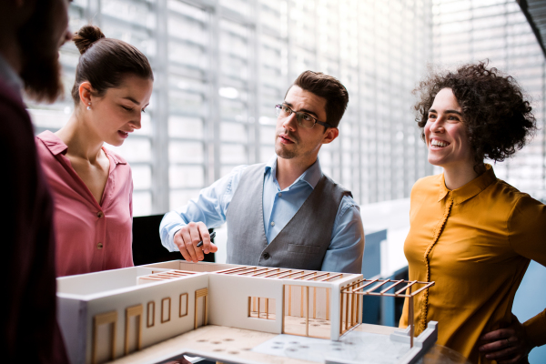 A group of young architects with model of a house standing in office, working and talking.