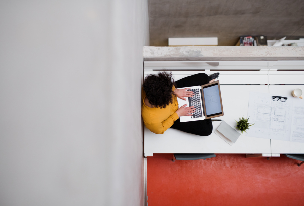 A top view of young businesswoman or architect sitting on desk in an office, using laptop. Copy space.