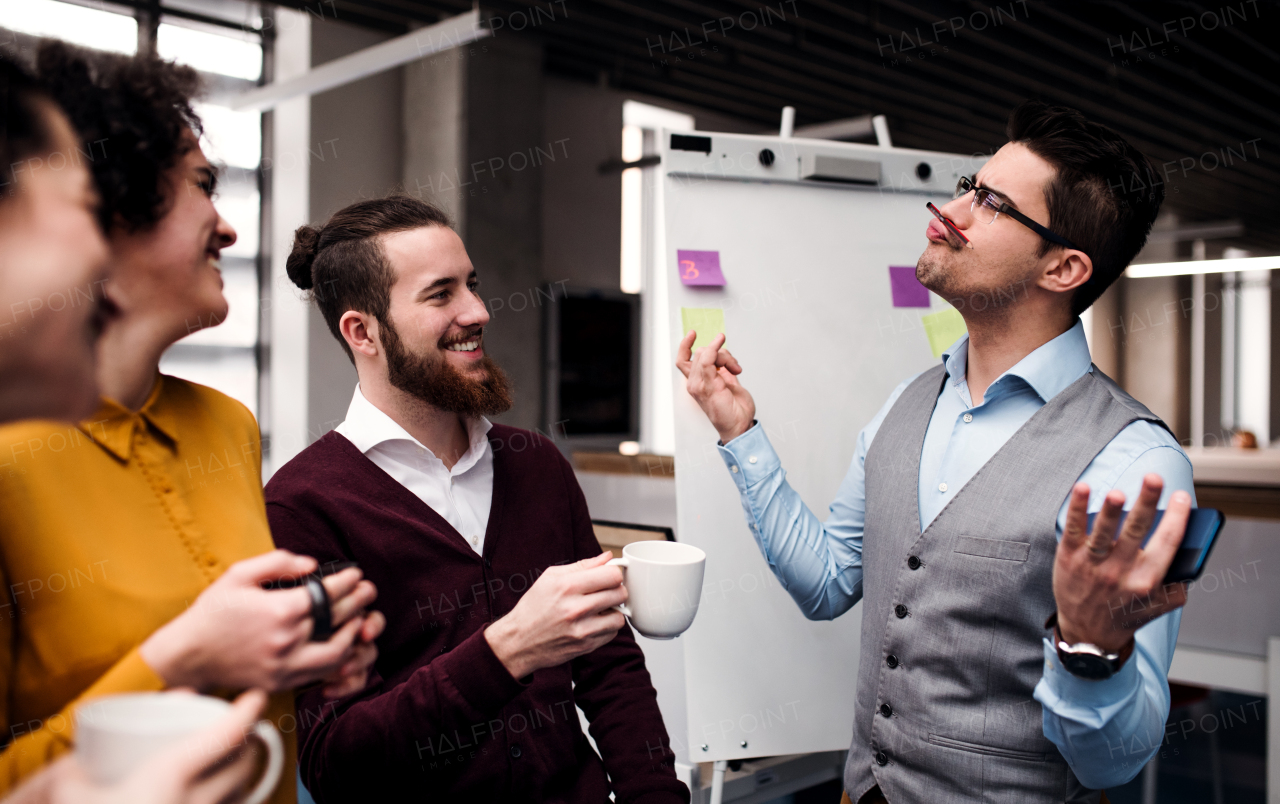 A group of cheerful young businesspeople with cup of coffee standing in office, having fun.