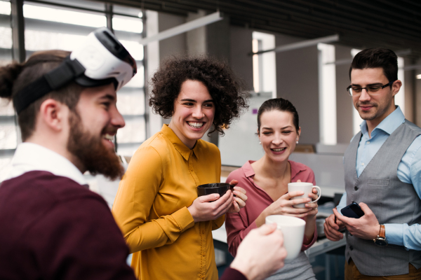 A group of young businesspeople with VR goggles standing in office, talking.