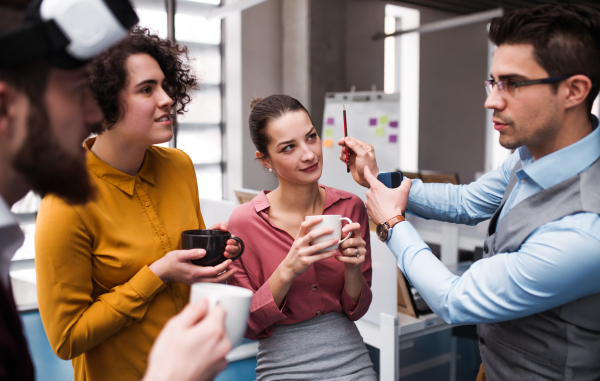 A group of cheerful young businesspeople with cup of coffee standing in office, talking.