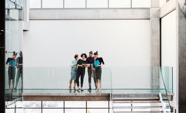 A group of young businesspeople standing near a staircase, talking.