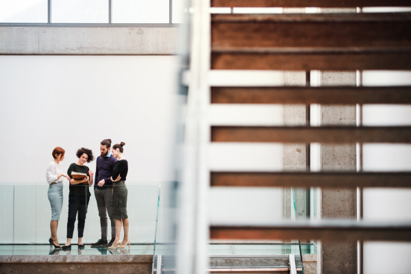 A group of young businesspeople standing near staircase, talking.