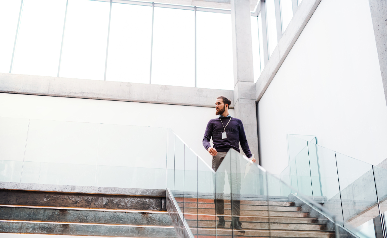 A young businessman walking down the stairs in office building. Copy space.