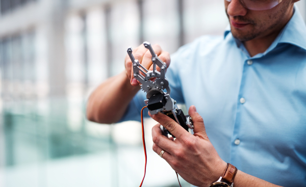 A midsection of young businessman or scientist with robotic hand and safety glasses standing in office, working.