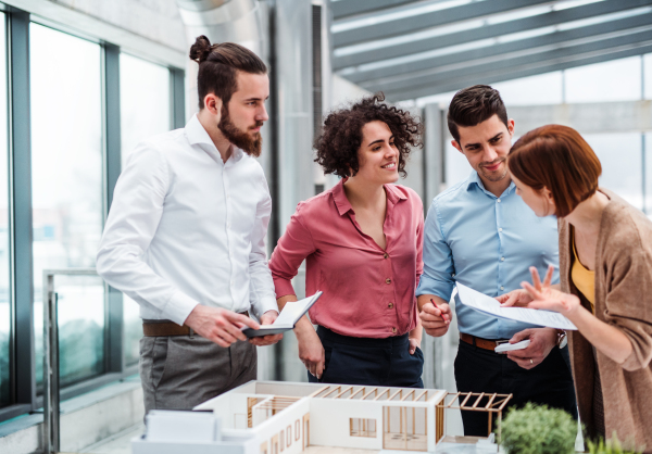 A group of young architects with model of a house working in office, talking.