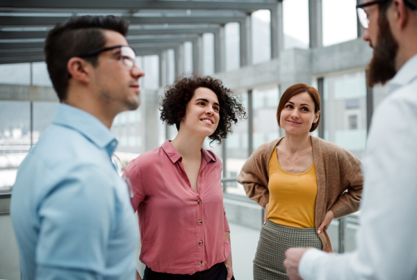 A group of cheerful young businesspeople standing in office, talking.