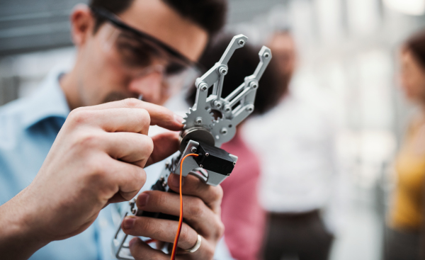 A young businessman or scientist with robotic hand and safety glasses standing in office, working.