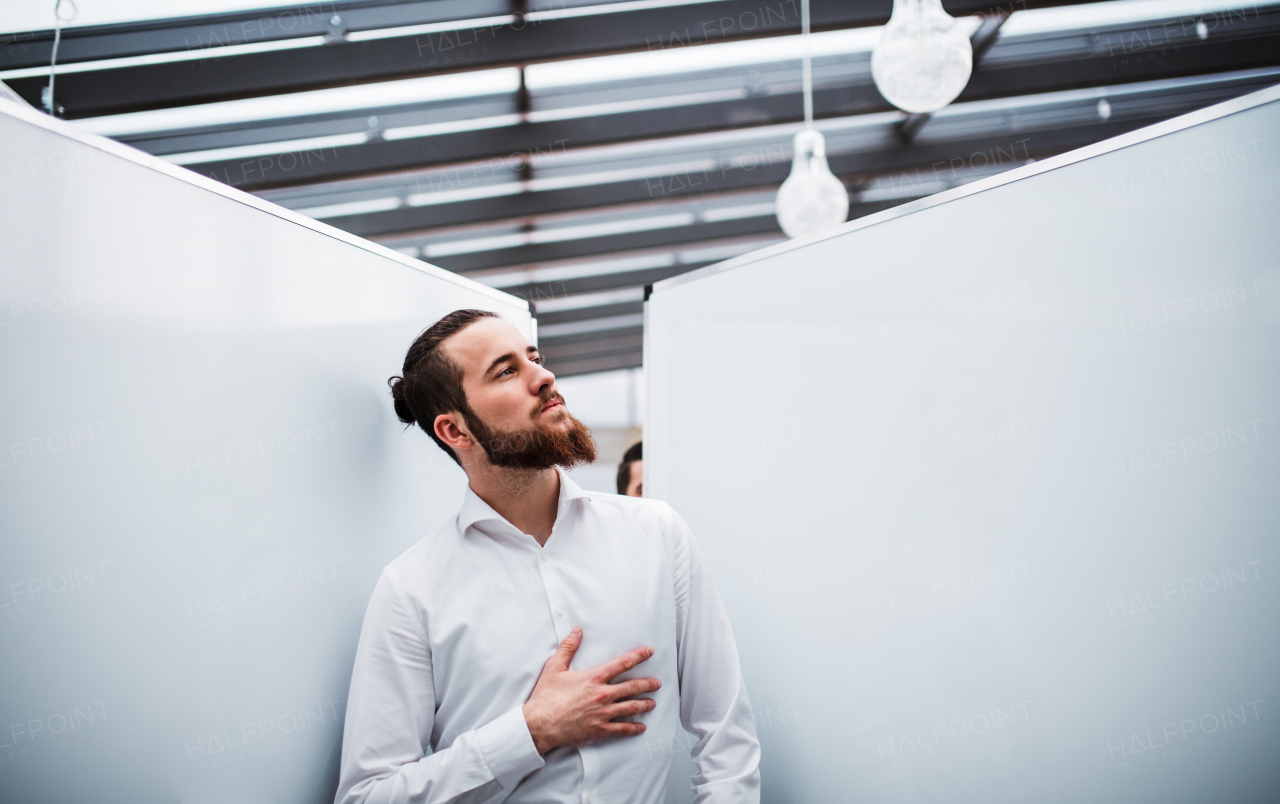 A young hipster businessman with white shirt standing in office.