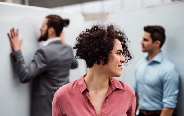 A portrait of young businesswoman standing in office, colleagues in the background.