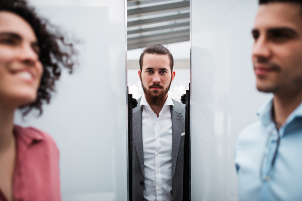 A portrait of young businessman in suit with colleagues standing in office.