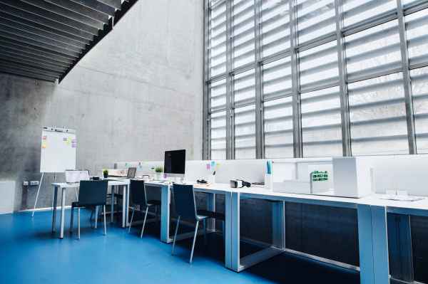 An interior of desks with computer and model of a house in modern spacious office.