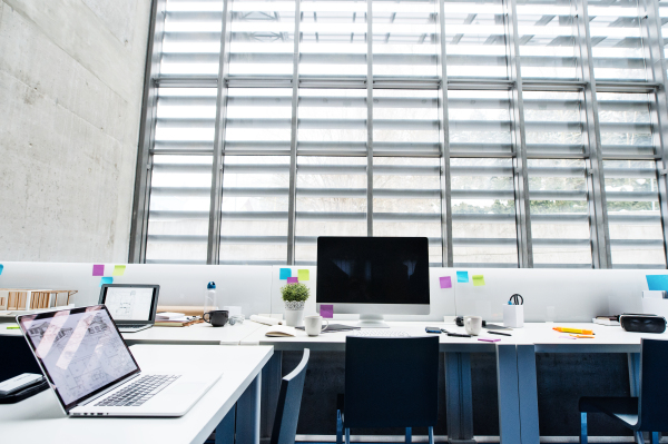 An interior of desks with computer and model of a house in modern spacious office.