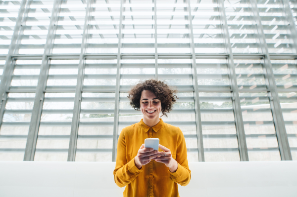 Portrait of a young student or businesswoman with smartphone in a library or office. Copy space.